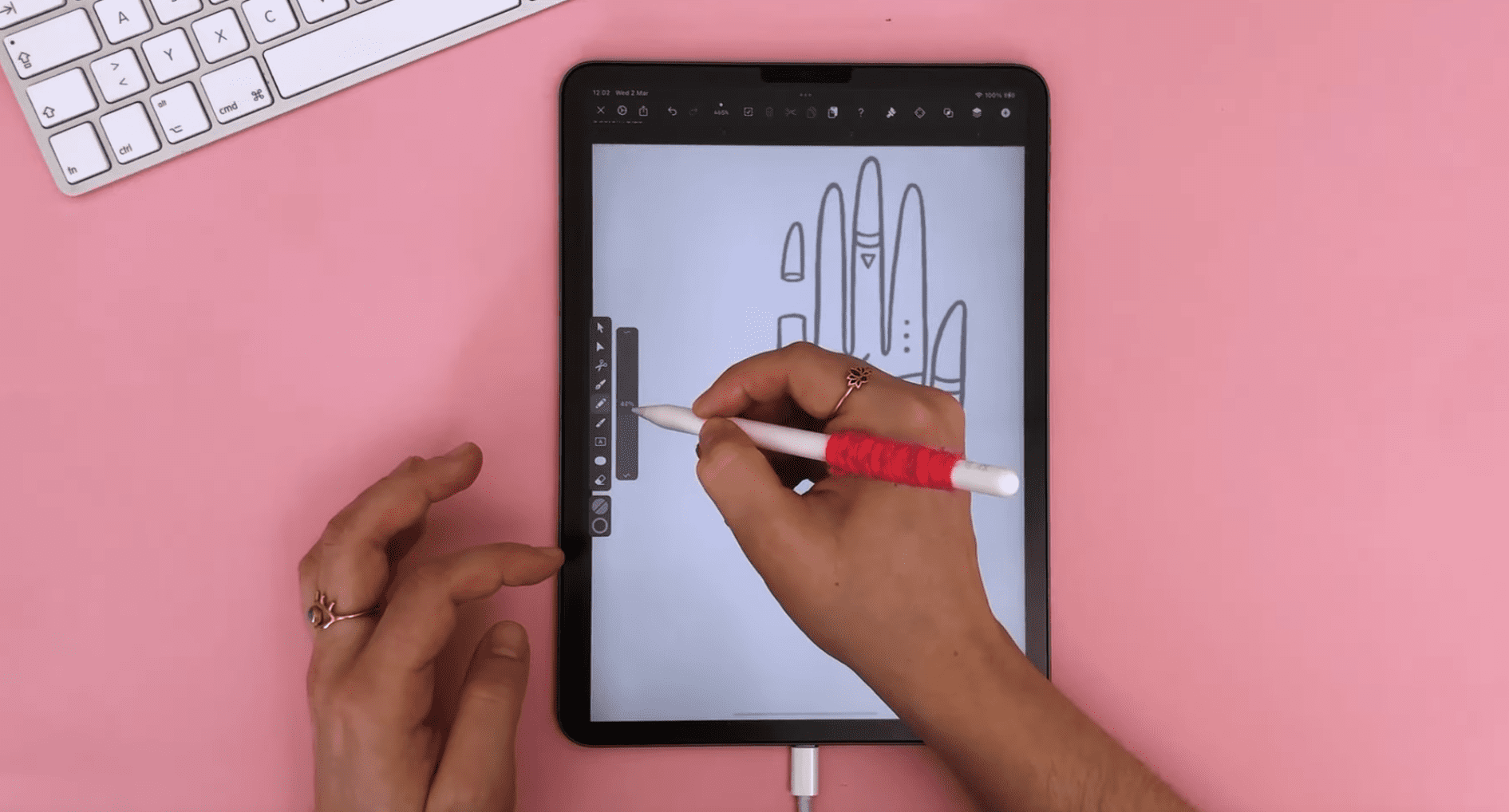 Female hands drawing on iPad with a pink background.
